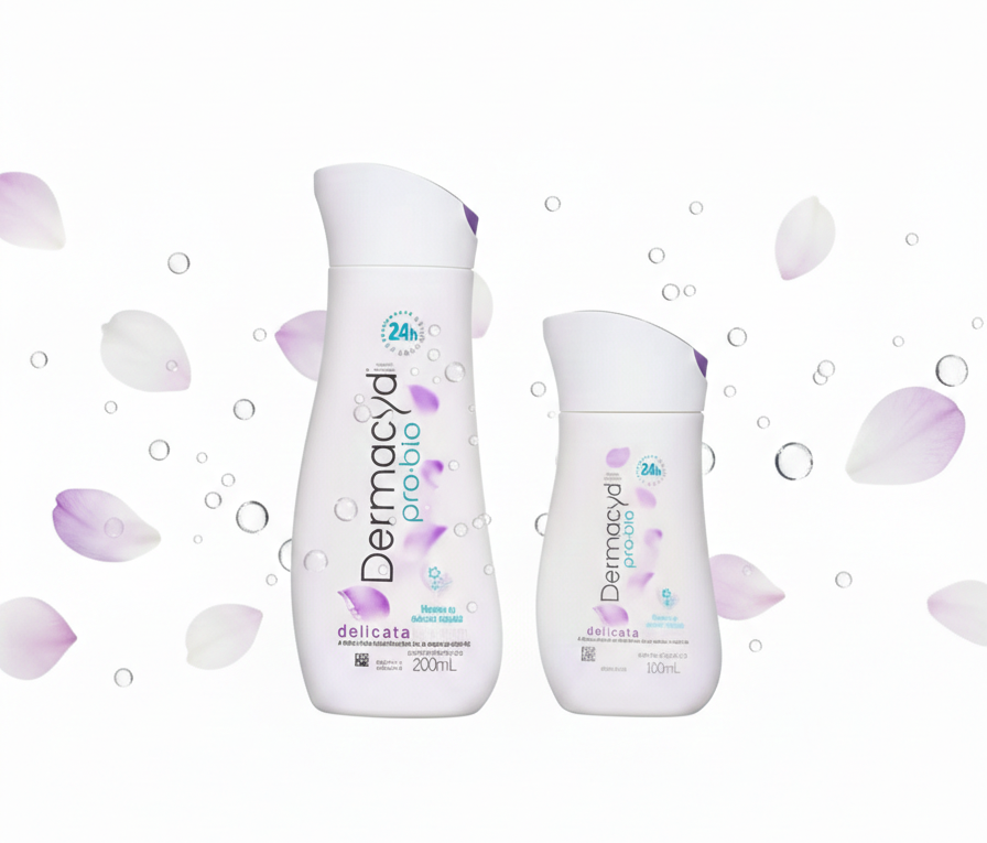 Duas embalagens do sabonete íntimo Dermacyd Pro-bio Delicata (200ml e 100ml) centralizadas em um fundo branco limpo, com pétalas de flores lilás e bolhas de água suaves flutuando ao redor, em formato horizontal para destaque de blog.