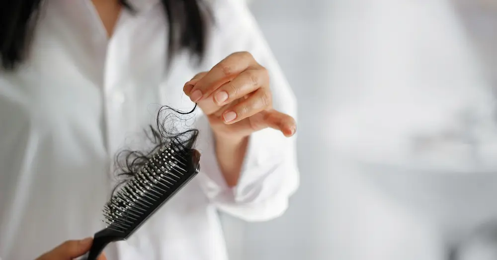Mulher preocupada com a queda de cabelo feminina ao olhar os fios na escova.
