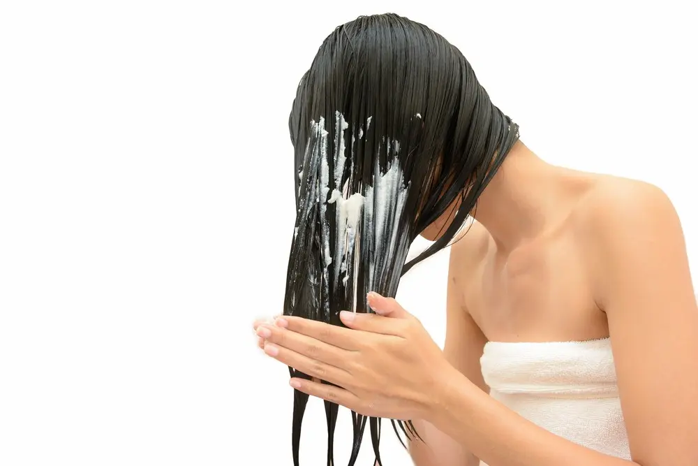 Mãos aplicando máscara de hidratação e enluvando uma mecha de cabelo úmido.