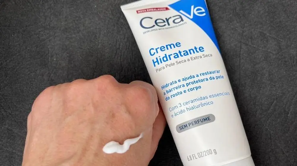 Close detalhado da textura consistente e branca do creme hidratante CeraVe sendo aplicada na pele.