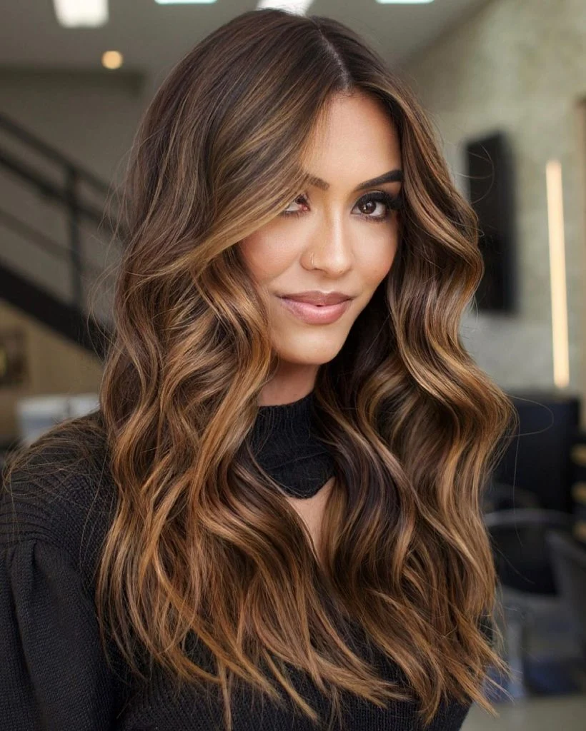 Mulher sorrindo com cabelo longo ondulado morena iluminada em tons de caramelo e avelã, mostrando o resultado final de cuidados capilares.