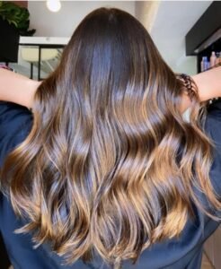 Cabelo longo ondulado com técnica Morena Iluminada em tons de mel e caramelo, mostrando brilho intenso e saúde dos fios.