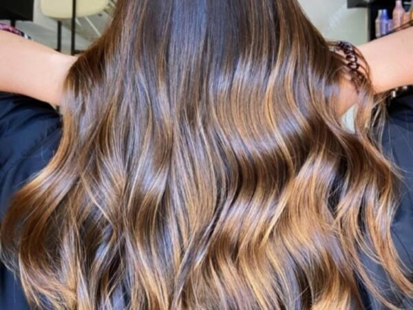 Cabelo longo ondulado com técnica Morena Iluminada em tons de mel e caramelo, mostrando brilho intenso e saúde dos fios.