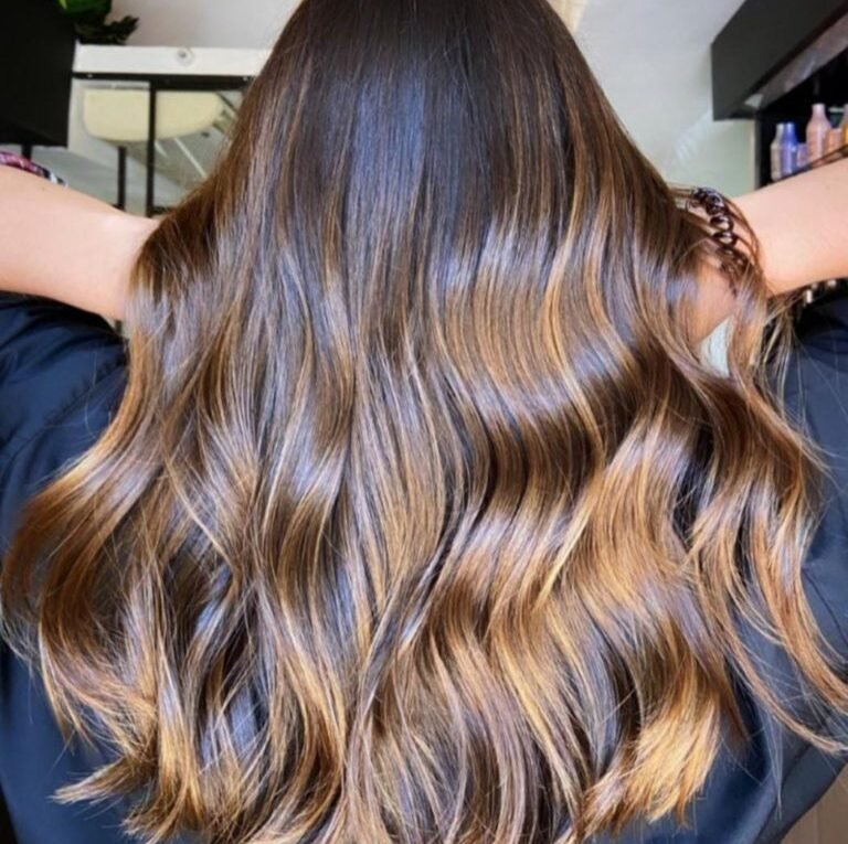 Cabelo longo ondulado com técnica Morena Iluminada em tons de mel e caramelo, mostrando brilho intenso e saúde dos fios.