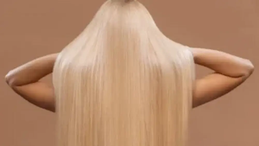 Foto de costas de uma mulher com cabelos longos, loiros e extremamente lisos e brilhantes. O cabelo está com aparência saudável e sedosa, representando o resultado final após o tratamento de recuperação capilar.