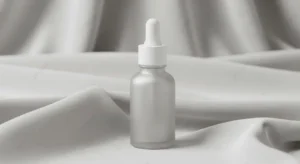 Frasco de sérum facial minimalista em vidro fosco sobre tecido de seda cinza, representando cuidados com a pele sem fragrância.