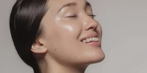 Modelo com pele iluminada e saudável tocando o rosto com as mãos, representando o resultado da recuperação da barreira cutânea.