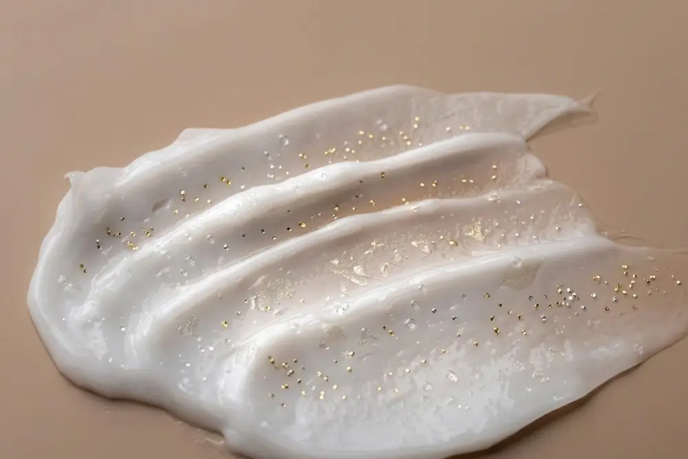 Amostra macro de textura de creme hidratante facial denso e branco espalhado sobre um fundo bege clean, destacando a hidratação profunda.